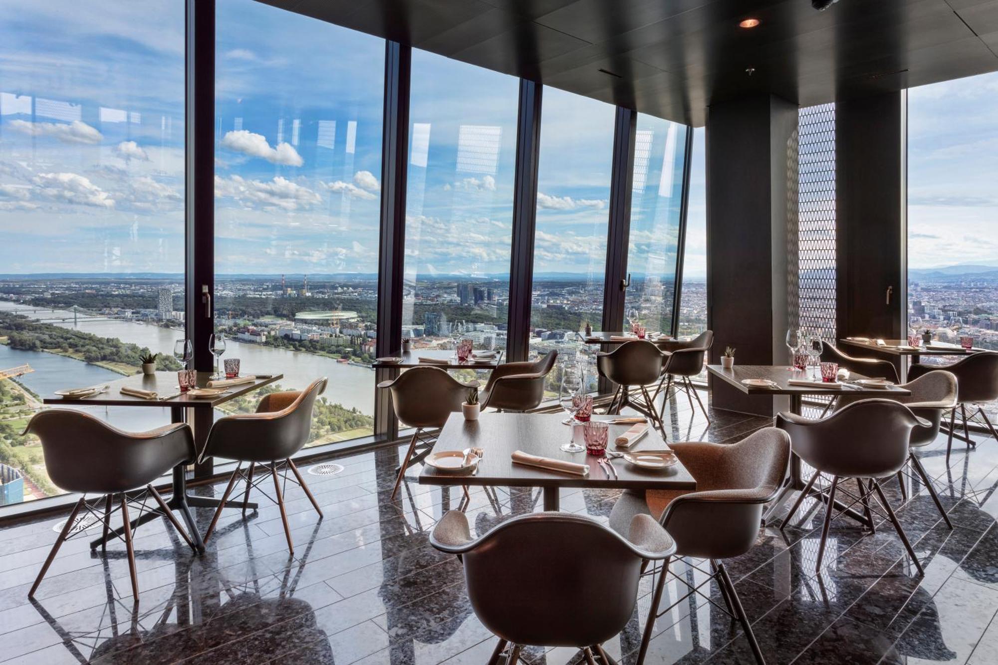เมเลีย เวียนนา Hotel ภายนอก รูปภาพ The photo shows a modern dining space with a sleek design, featuring several tables and chairs arranged near large floor-to-ceiling windows. These windows provide a panoramic view of a river and surrounding landscape. The dining area has a contempora