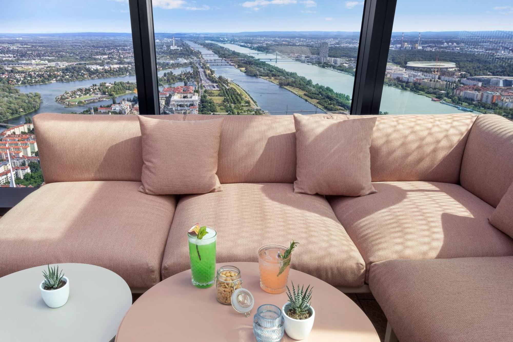 เมเลีย เวียนนา Hotel ภายนอก รูปภาพ The photo shows a cozy seating area with a large, soft, light pink couch and some small decorative pillows. In front of the couch, there is a round table with a few drinks placed on it: a green cocktail with a garnish, a light pink drink, and some sn