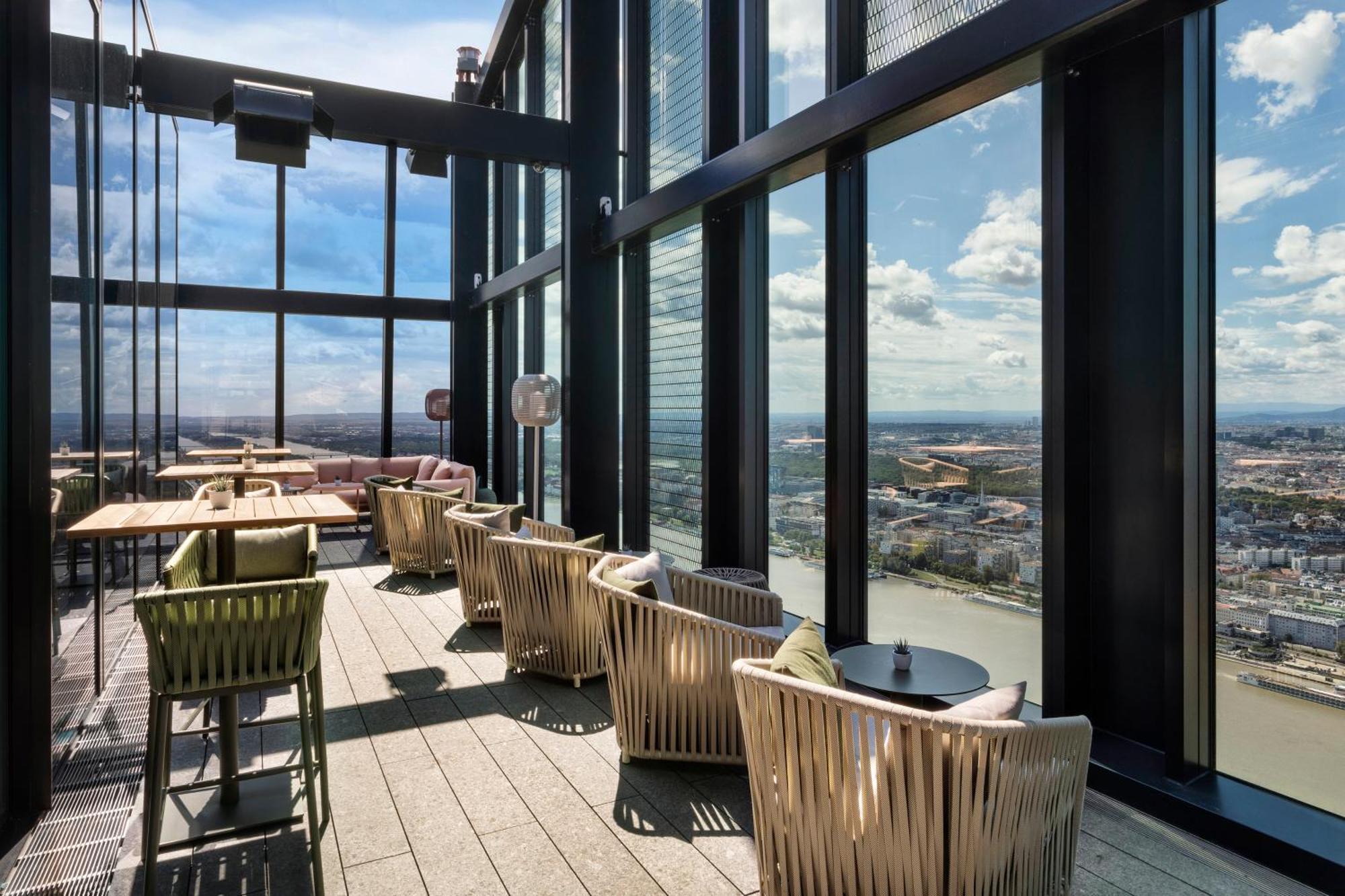 เมเลีย เวียนนา Hotel ภายนอก รูปภาพ The image shows a stylish indoor space with large floor-to-ceiling windows that provide a panoramic view of the landscape outside. The area features several comfortable seating arrangements, including modern chairs and small tables. The design is sle