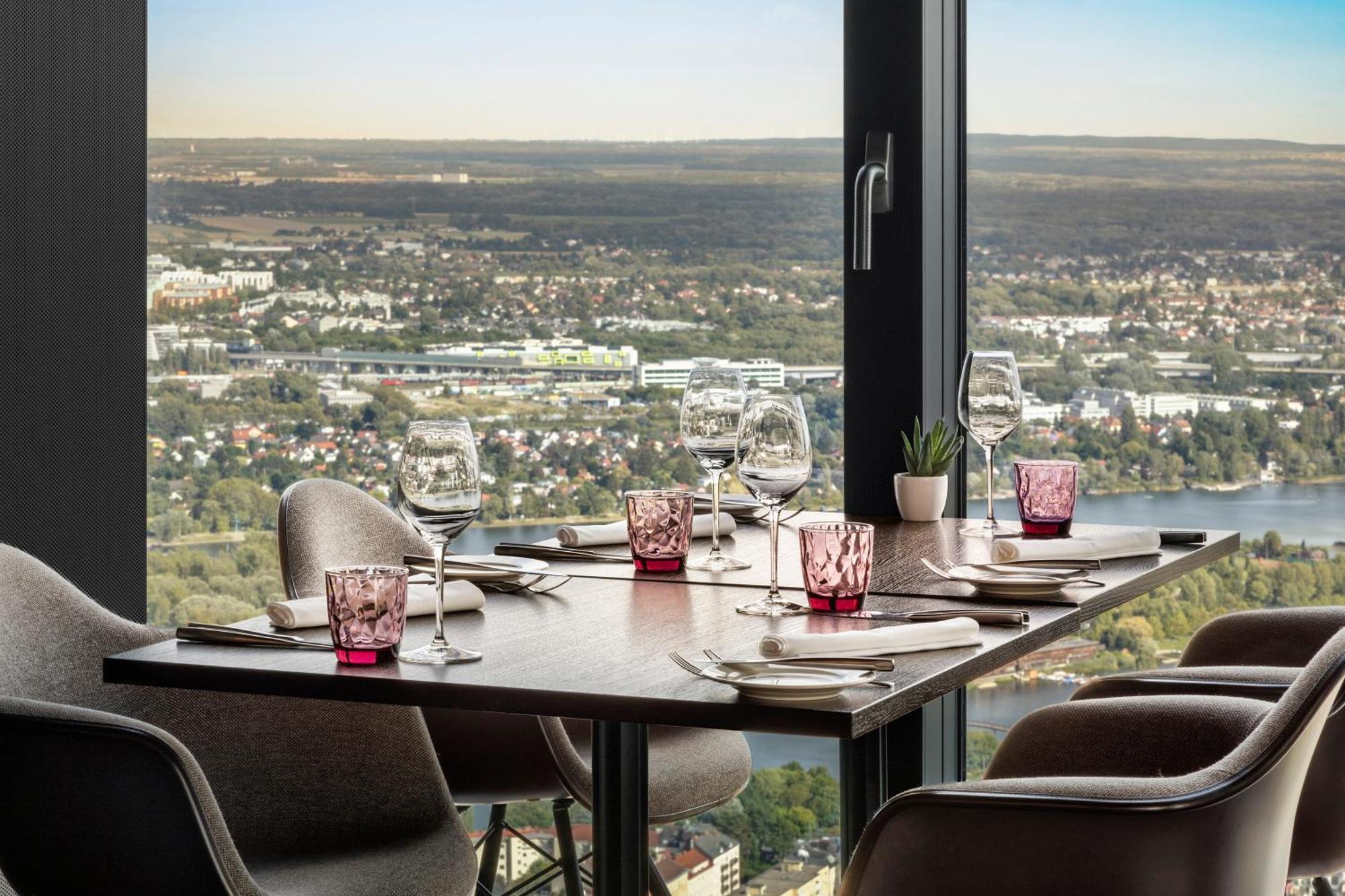 เมเลีย เวียนนา Hotel ภายนอก รูปภาพ The photo shows a dining table set up in a restaurant with a view. The table has dark wood and features several dining essentials arranged neatly. There are elegant wine glasses, pink-tinted glass holders, and plates set beside them. A small plant is