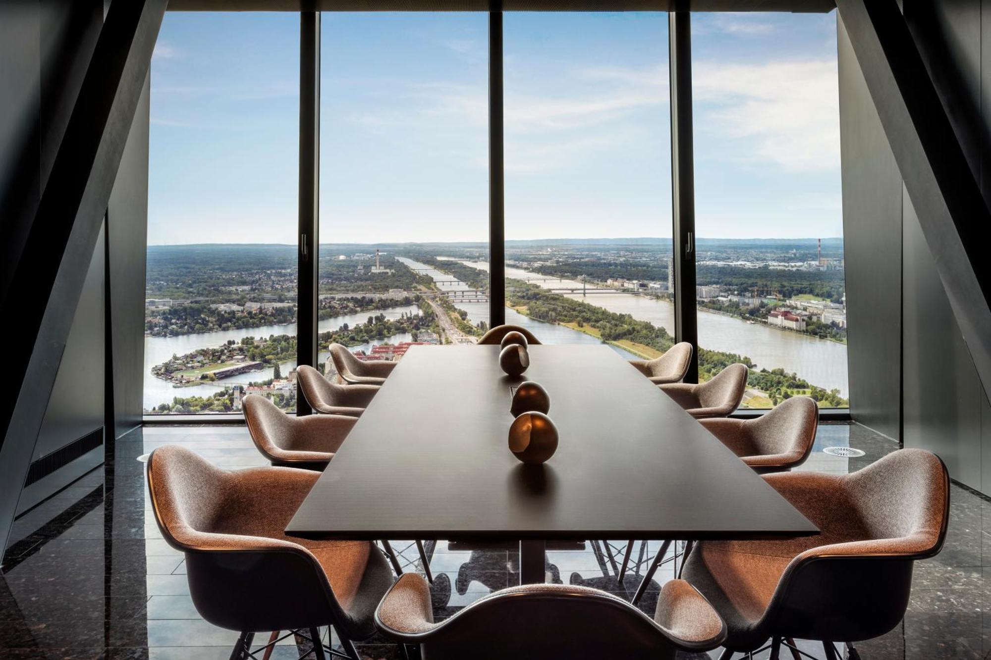 เมเลีย เวียนนา Hotel ภายนอก รูปภาพ The photo depicts a modern conference room with a long table surrounded by several stylish chairs. The room features large floor-to-ceiling windows that offer an expansive view of a landscape featuring water, greenery, and man-made structures in the 