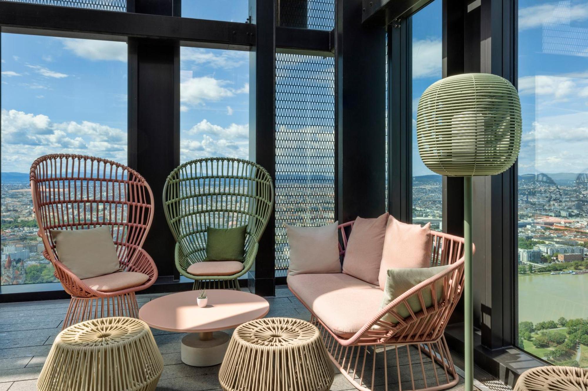 เมเลีย เวียนนา Hotel ภายนอก รูปภาพ The photo shows a modern lounge area with large windows offering a view of the outdoors. There are two stylish, high-backed chairs made of wicker in pastel colors—one pink and one green. A cozy sofa in a soft pink hue is positioned between them, acco